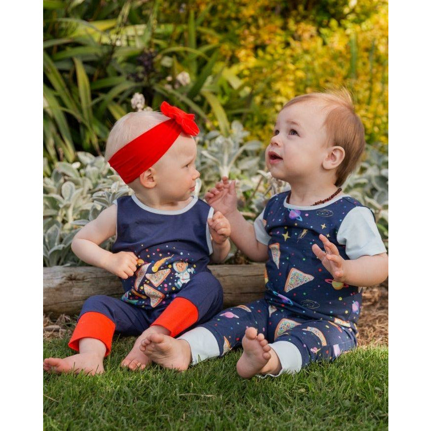 two little toddlers sitting on grass wearing colourful romperoos rompers looking at each other