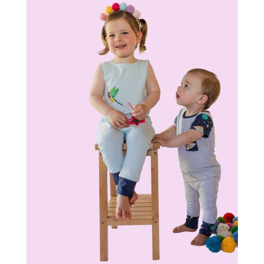 little girl toddler sitting on chair with little boy standing next to her, both modelling a leon and bird romperoo romper